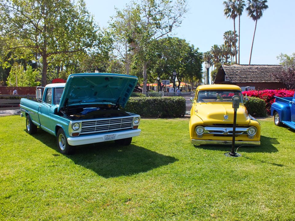 Teal Ford pickup with open hood beside a yellow vintage pickup on grass