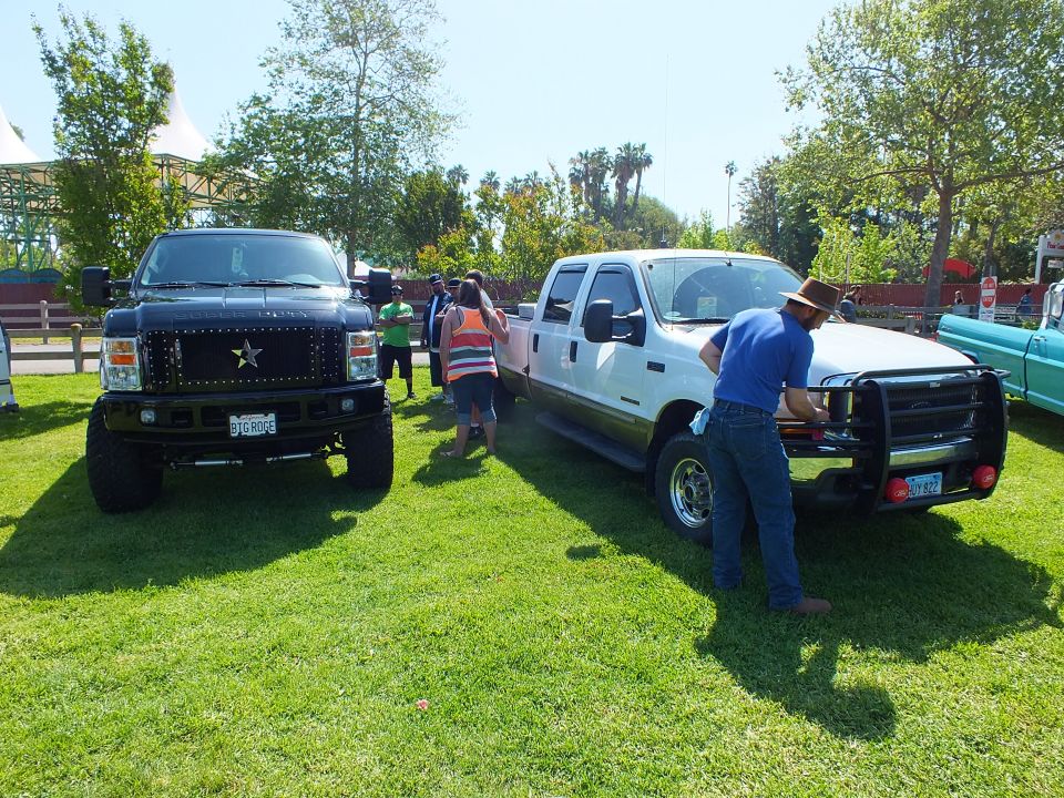 Black lifted truck and white crew-cab pickup at a car show, people nearby