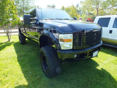 2003 Ford Crown Victoria - Side-front view of a black lifted Ford Super Duty with chrome star grille and large mud tires parked on grass at a show.
