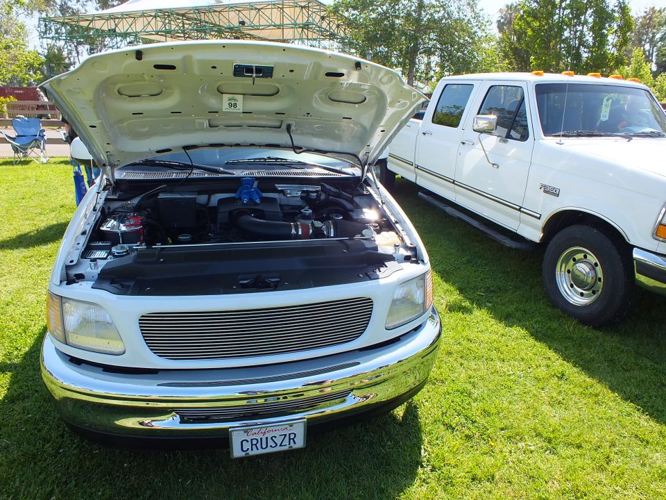White truck with open hood and billet grille beside white Ford crew cab