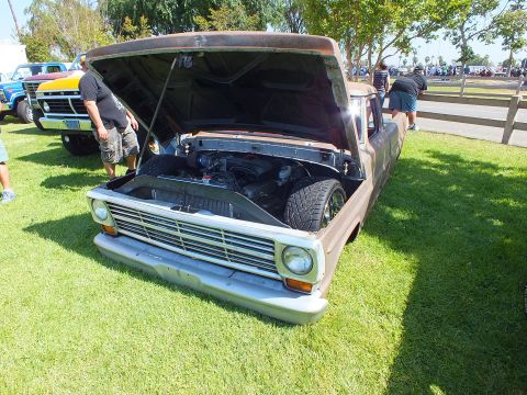 2003 Ford Crown Victoria - bare-metal patina Ford F-series pickup displayed hood-up on grass, with people and other show vehicles in the background.