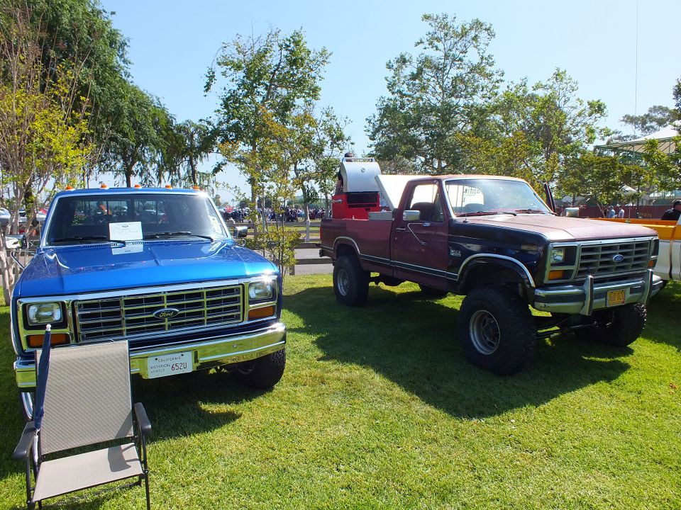 blue squarebody Ford pickup and a lifted maroon Ford 4x4 parked on grass at an outdoor car show