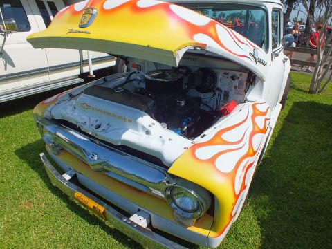 2003 Ford Crown Victoria - Front of a flame-painted 1950s Ford F-100 with the hood raised, revealing a Chevrolet small-block V8 engine swap.