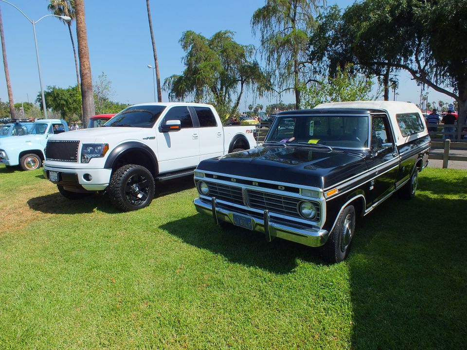 white modern Ford F-150 and a black 1970s Ford pickup with camper shell parked on grass