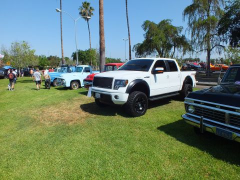 2003 Ford Crown Victoria - white lifted Ford F-150 FX4 crew cab on black wheels parked on show grass with other vehicles and palms behind.