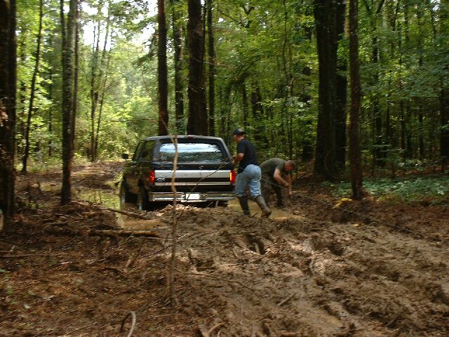 1995 Ford Bronco rear view stuck in mud with two people attempting recovery