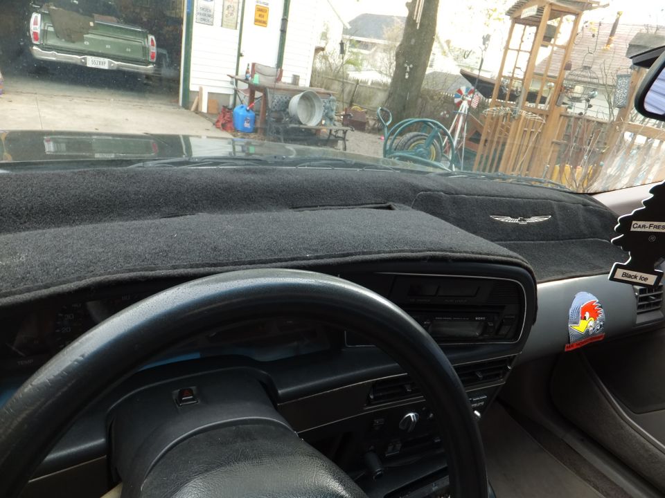 Driver's view over a black carpeted dash cover with bird emblem, Sony CD stereo, and green hood ahead