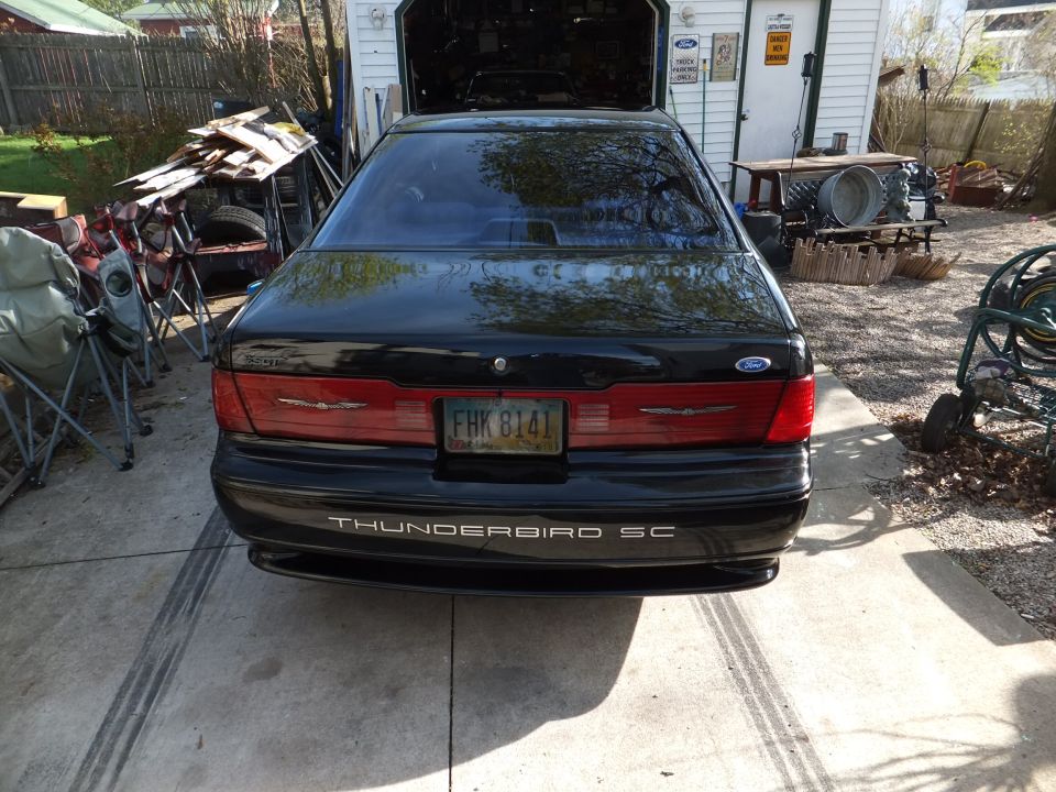 Rear of black Ford Thunderbird SC parked in driveway near open garage