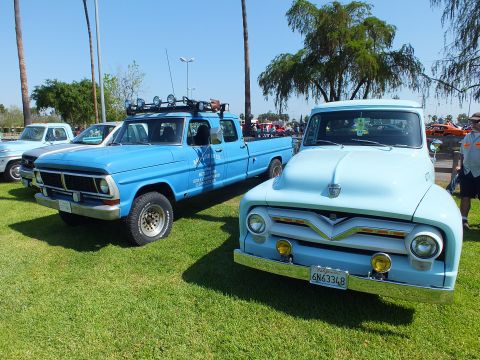 2003 Ford Crown Victoria - blue lettered 1970s Ford crew-cab work truck with roof lights parked beside a light blue 1955 Ford F-100 at a car show.