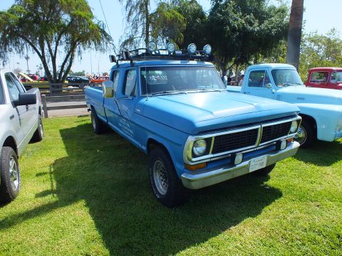 2003 Ford Crown Victoria - blue 1970s Ford extended-cab pickup fitted with a roof light bar and lettered doors, parked on show grass among other trucks.