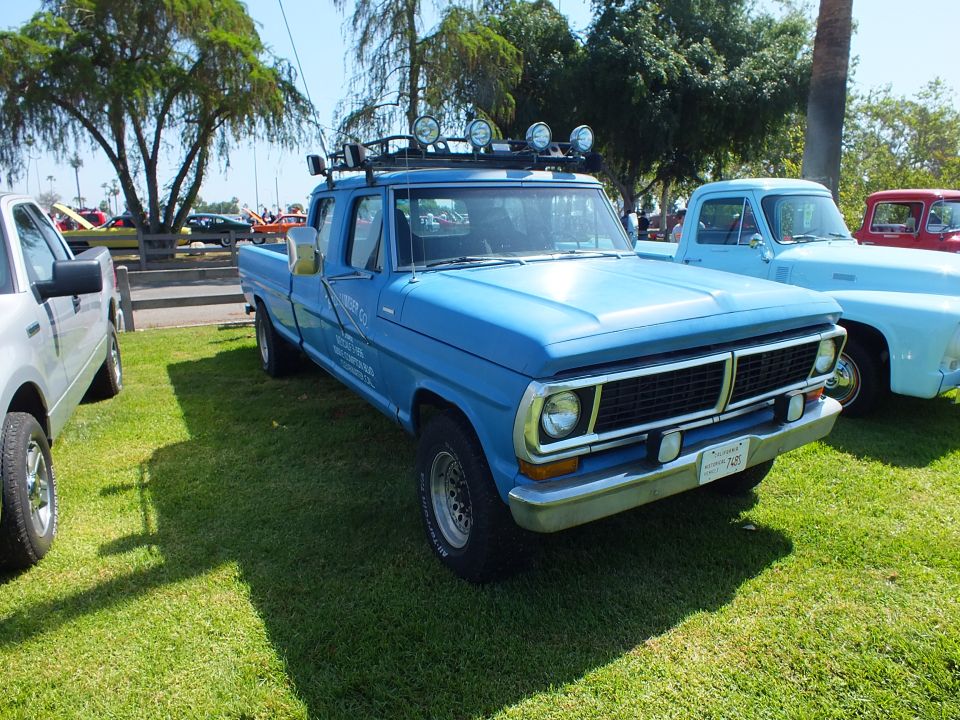 blue 1970s Ford extended-cab pickup with roof light bar parked on grass at a car show