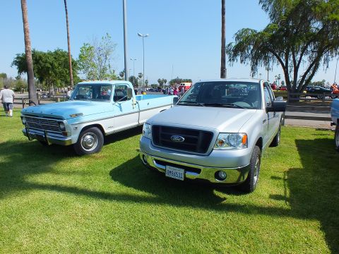 2003 Ford Crown Victoria - light blue 1970s Ford pickup parked beside a silver mid-2000s Ford F-150 with a black mesh grille on sunny show grass.