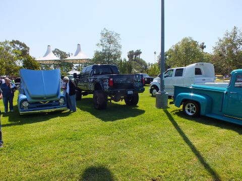 2003 Ford Crown Victoria - car-show lawn showing a hood-up light blue 1950s Ford, a black lifted modern Ford and a teal 1950s Ford F-100 stepside.