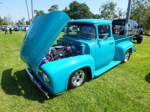 2003 Ford Crown Victoria - restored teal-blue classic pickup sits on grass with its hood raised, exposing a chromed and purple-accented engine at a car show.