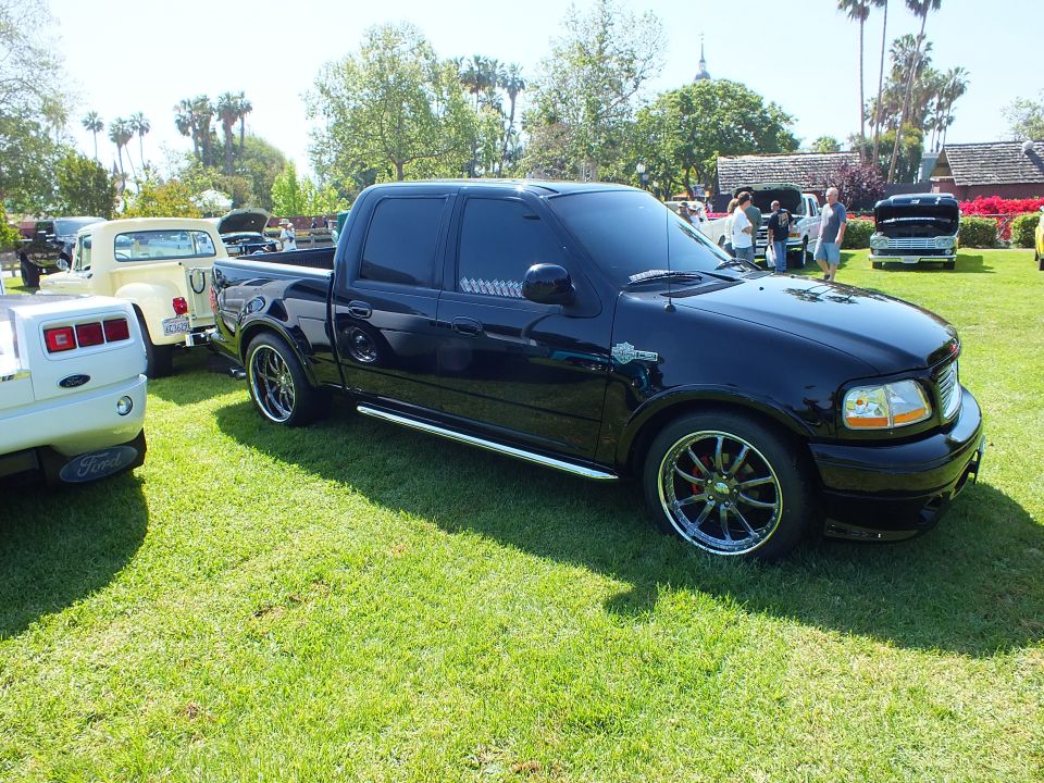 Black crew-cab pickup truck with chrome wheels parked on grass at car show