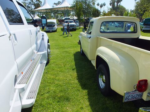 2003 Ford Crown Victoria - cream-colored vintage stepside pickup is parked on grass next to a white dually truck with chrome running boards at a car show.