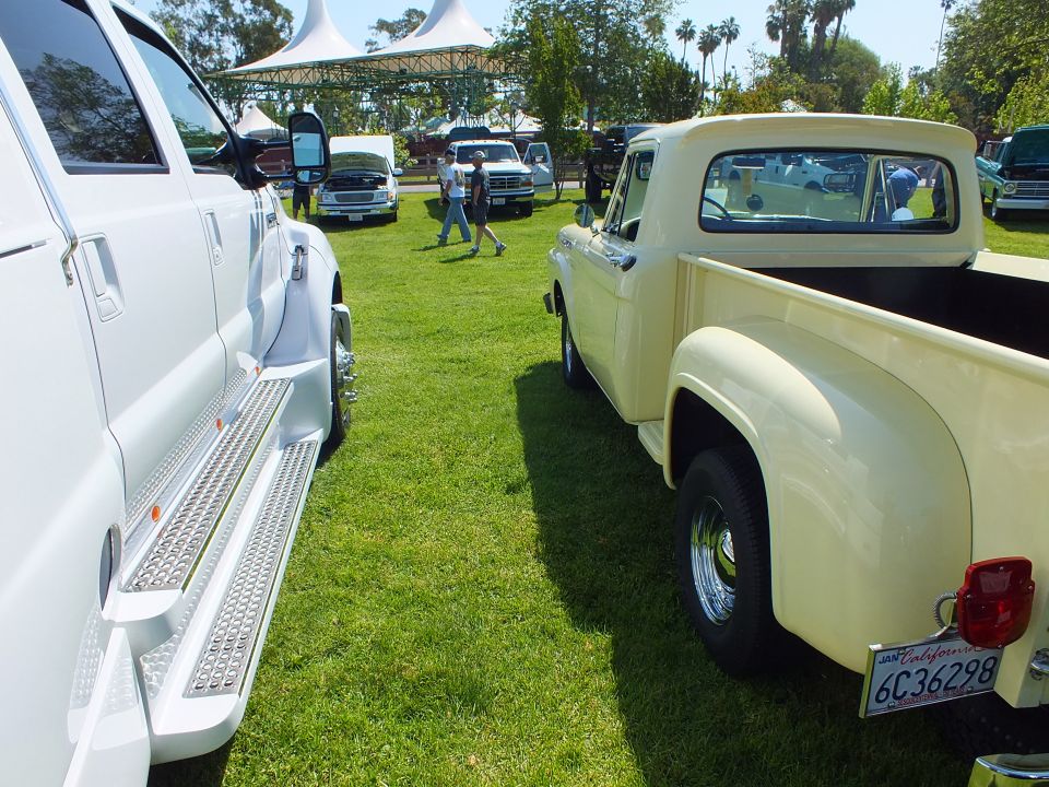 Cream vintage stepside pickup beside white dually with running boards at show