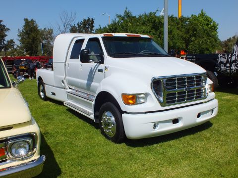 2003 Ford Crown Victoria - white custom crew-cab dually with a large chrome grille and CAT badge sits on a show lawn next to a cream vintage truck.
