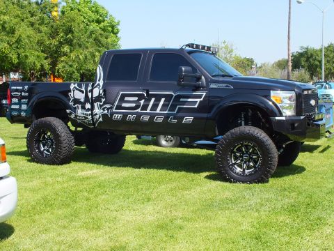 2003 Ford Crown Victoria - Side view of a black lifted crew-cab truck with BMF Wheels skull graphics, large off-road tires, and a roof light bar on a lawn.