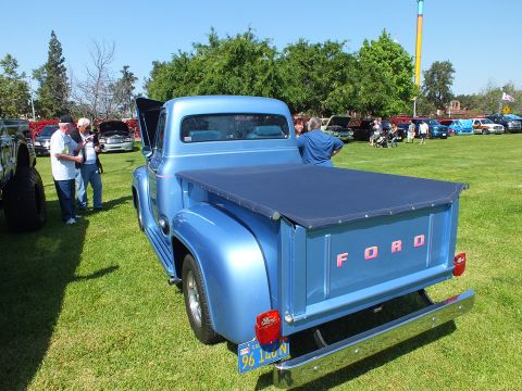 2003 Ford Crown Victoria - metallic-blue classic Ford pickup with a soft bed cover and red FORD lettering on the tailgate is shown on grass as people browse.