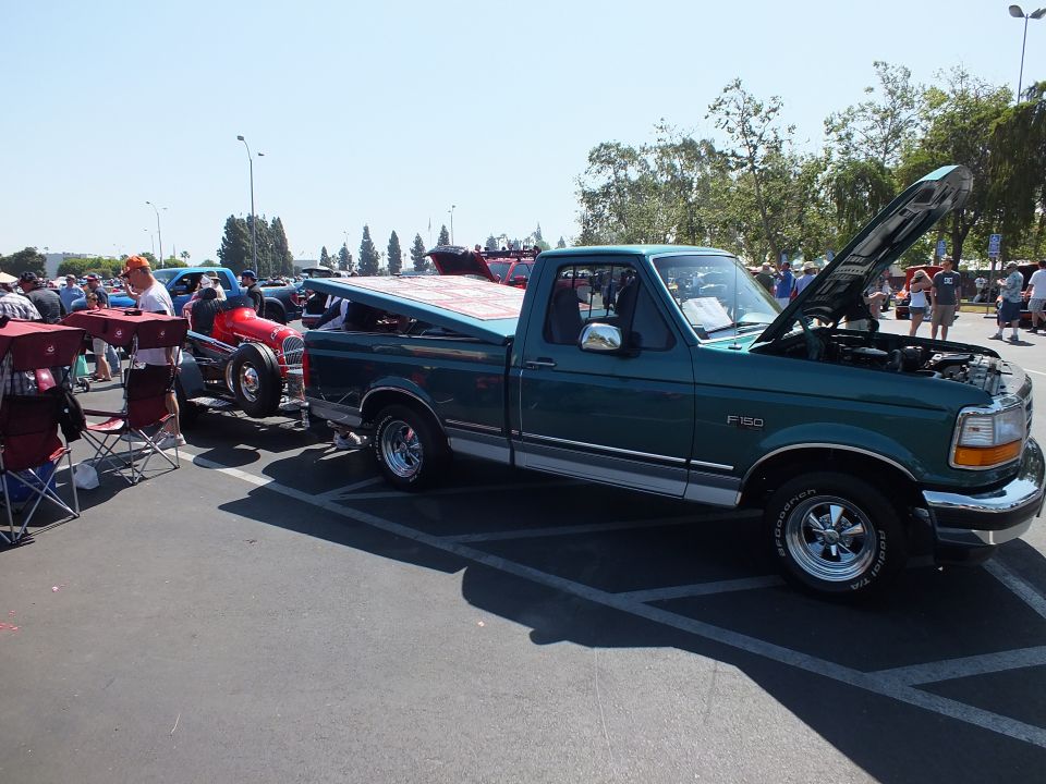 Green Ford F-150 pickup with open hood at paved car show next to red hot rod