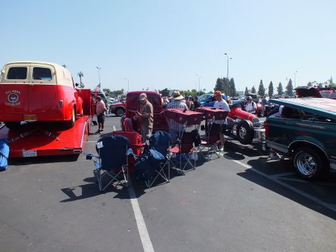2003 Ford Crown Victoria - red Gilmore-lettered vintage truck sits on a trailer surrounded by folding chairs and spectators at a crowded paved car show.