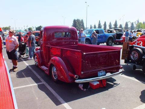 2003 Ford Crown Victoria - deep maroon vintage hot rod stepside pickup with chrome wheels is displayed at a busy paved car show as people walk past.