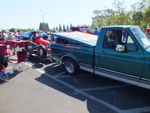 2003 Ford Crown Victoria - green Ford pickup is parked next to a red open-wheel hot rod at a paved car show with folding chairs and spectators around.