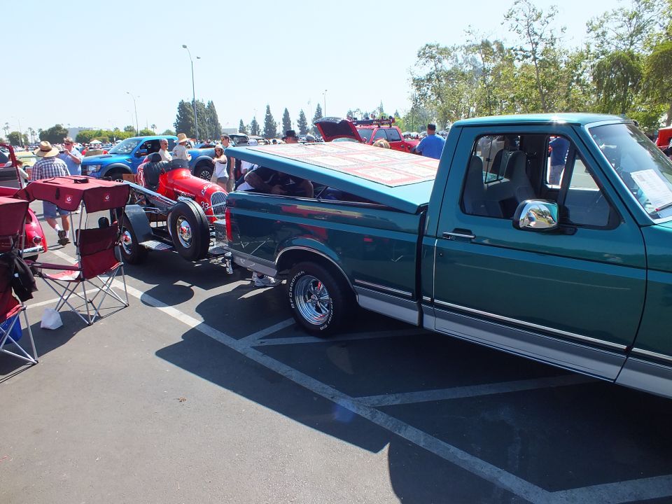 Green Ford pickup beside red open-wheel hot rod at paved car show