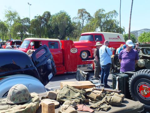 2003 Ford Crown Victoria - car show display of WWII military helmets, packs and gear laid out on a table in front of a red Gilmore panel truck and black hot rod.