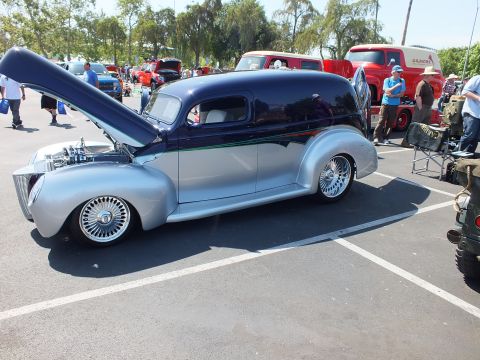 2003 Ford Crown Victoria - Side profile of a dark blue and silver custom sedan-delivery hot rod with chrome wire wheels and hood raised at a car show.