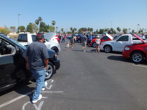 2003 Ford Crown Victoria - Spectators walk between rows of parked trucks and cars at an outdoor parking-lot car show on a sunny day.