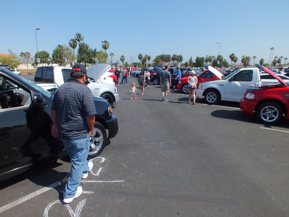 Crowded outdoor parking-lot car show with rows of trucks and people under a blue sky