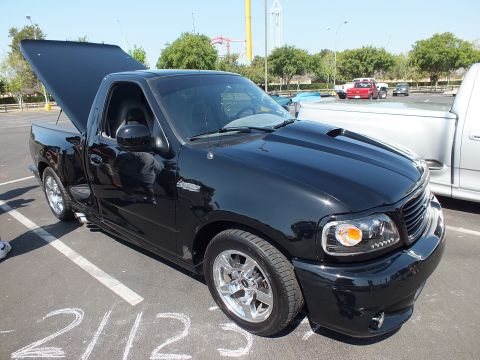 2003 Ford Crown Victoria - black Ford Lightning sport pickup with tailgate open sits at a car show, with chalk numbers marked on the pavement.