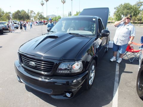 2003 Ford Crown Victoria - black Ford Lightning sport pickup shown front-on with raised tailgate and a man standing beside it at a car show.