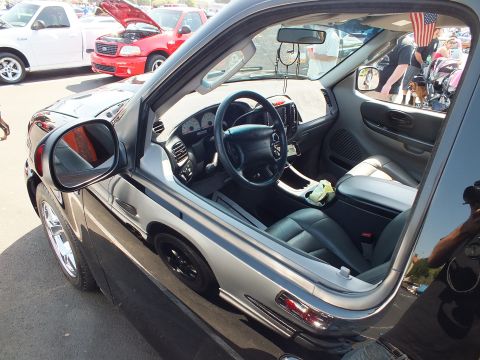 2003 Ford Crown Victoria - Interior of a black pickup seen through the open passenger window, showing the steering wheel, dash and gray leather seats.