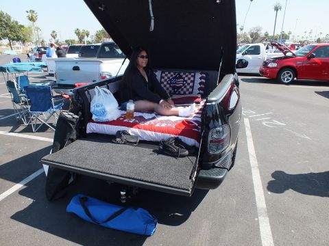 2003 Ford Crown Victoria - woman sits on red, white and blue bedding in the open bed of a black pickup with the tailgate down at a car show.