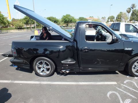 2003 Ford Crown Victoria - Side profile of a black single-cab sport pickup with hood raised and door open, parked at an outdoor car show.