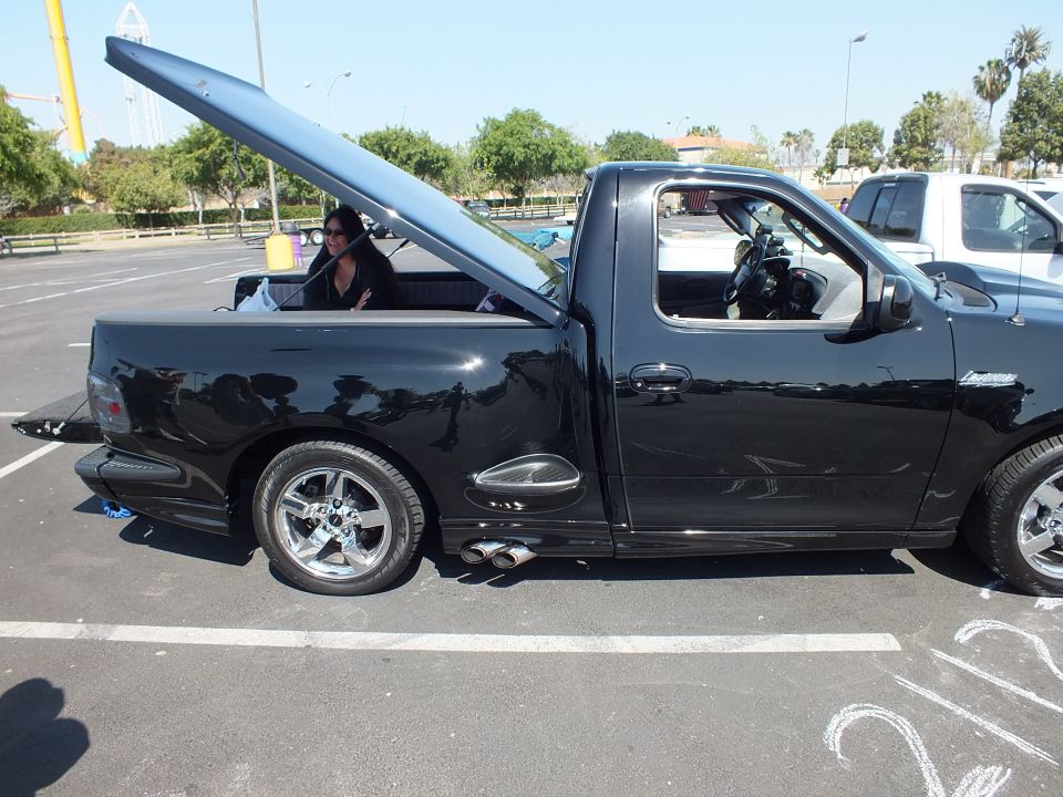 Side view of black single-cab pickup with raised hood and open door at car show