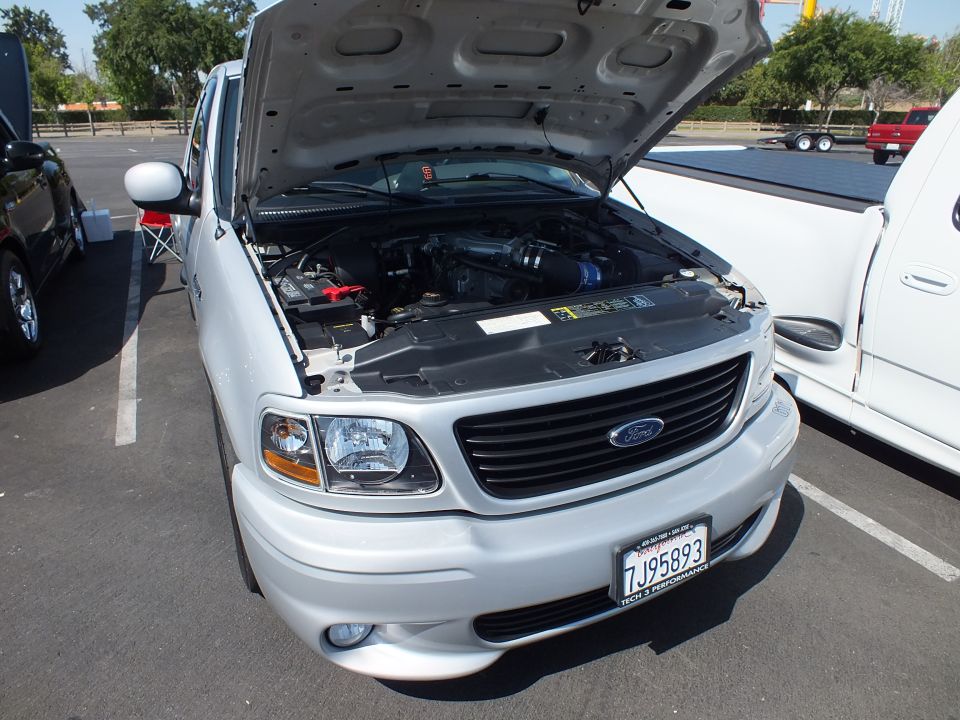 Engine bay and front of white Ford pickup with open hood and California plate 7J95893