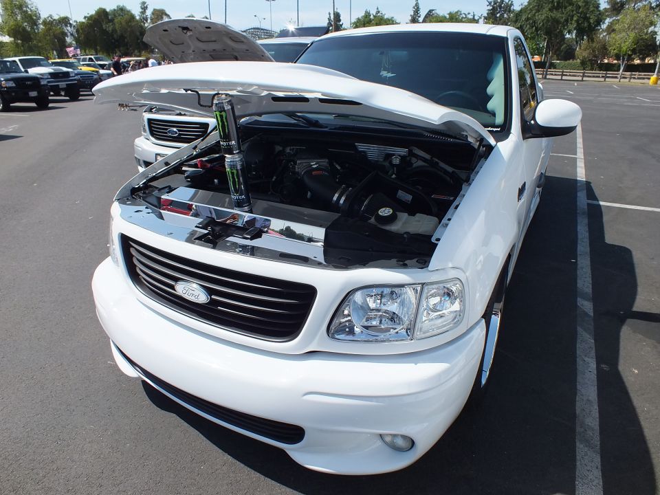 Front three-quarter of white Ford sport pickup with hood up showing engine at car show
