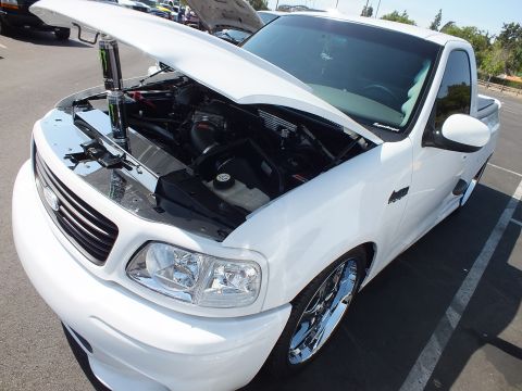 2003 Ford Crown Victoria - white Ford single-cab sport pickup, lowered on chrome wheels with hood raised to show the engine, at an outdoor car show.