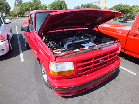2003 Ford Crown Victoria - red Ford pickup with hood raised shows its engine and California plate 871BOLT, a man standing beside it at a car show.