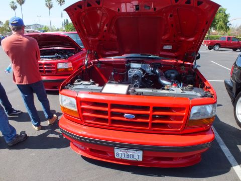 2003 Ford Crown Victoria - Front view of a red Ford pickup with hood raised showing the engine and California plate 871BOLT, with another red truck behind at a car sh…