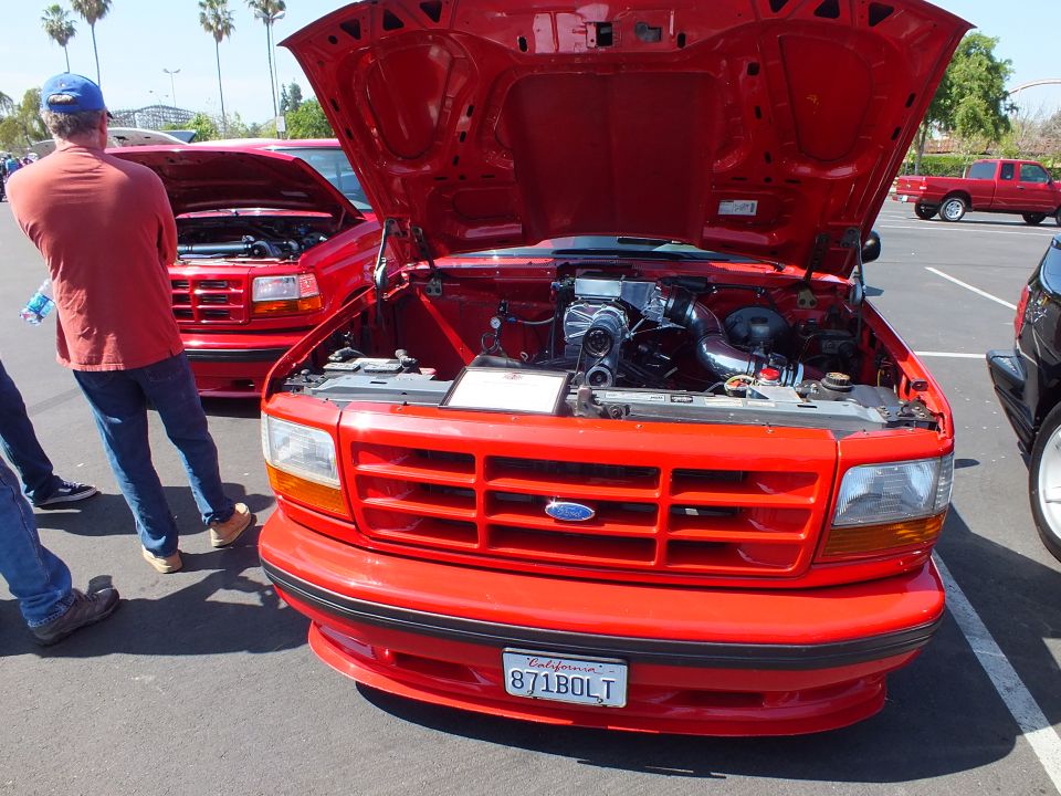 Red Ford pickup with open hood and California plate 871BOLT, second red truck behind it
