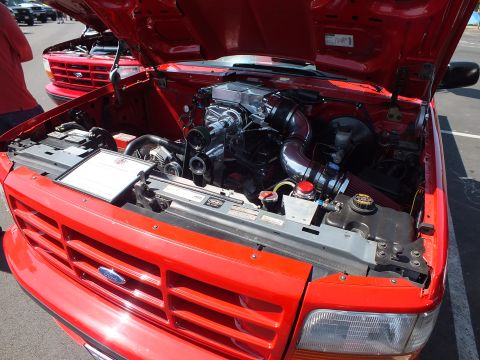 2003 Ford Crown Victoria - open engine bay of a red Ford pickup at a car show, with a supercharged V8 and a Ford oval on the front grille.