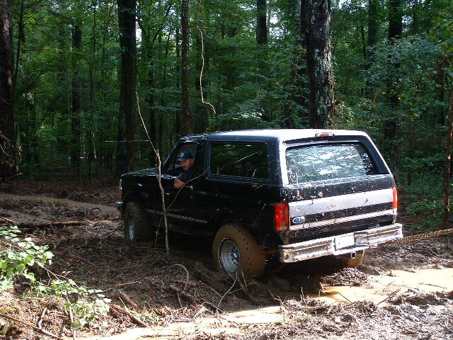Black 1995 Ford Bronco driving through mud in a forest