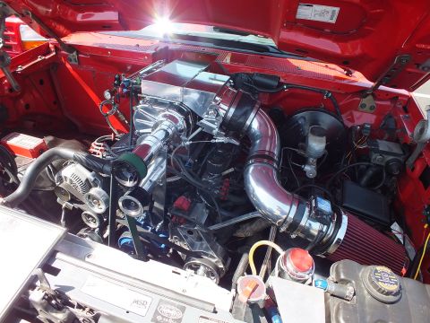 2003 Ford Crown Victoria - detailed look into a red truck's engine bay showing a supercharger, chrome intake piping and a cone air filter.