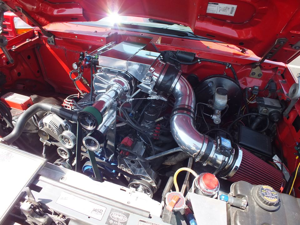 Modified engine bay of a red truck with polished supercharger, intake piping and cone air filter