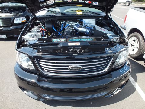 2003 Ford Crown Victoria - open engine bay of a black Lightning-style pickup with a supercharger, blue hoses and '2073' on the front bumper.